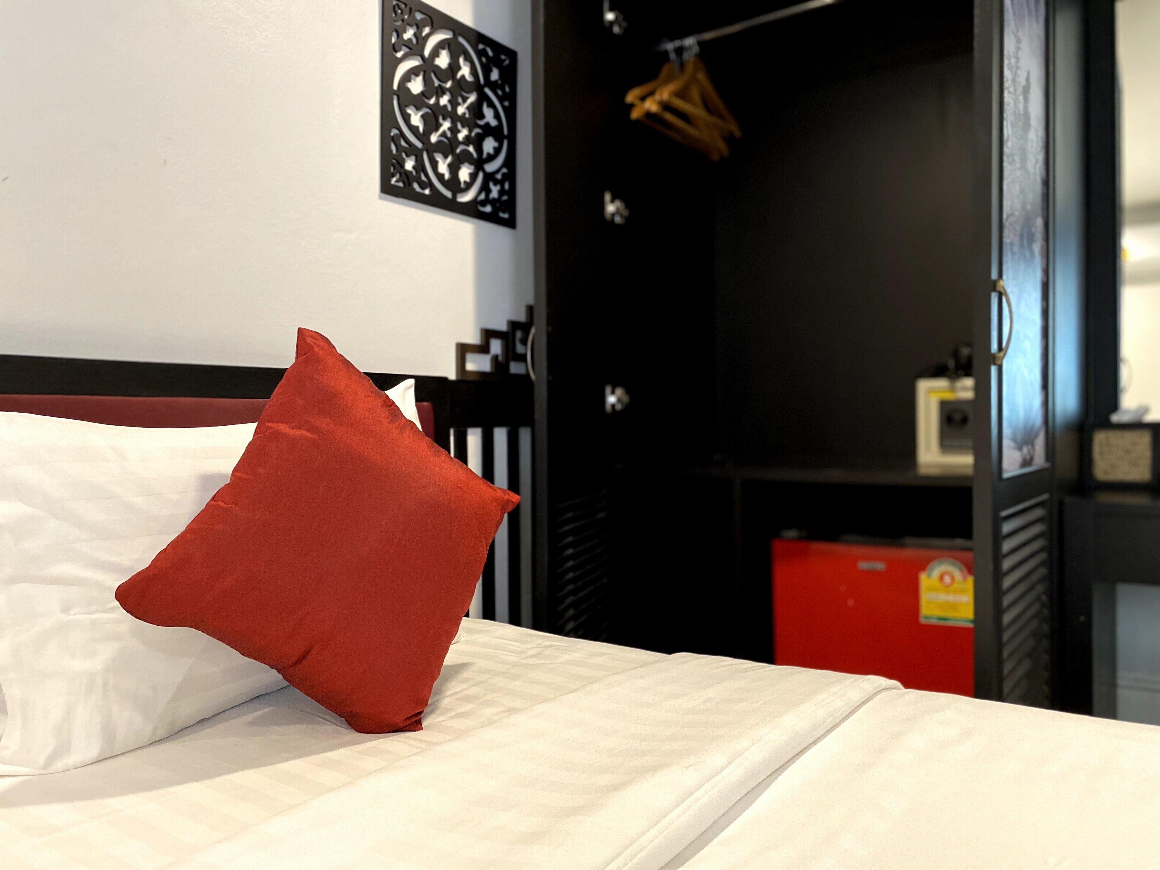 A bed with white bedding and a red pillow, a black headboard, and a wall with a decorative panel.