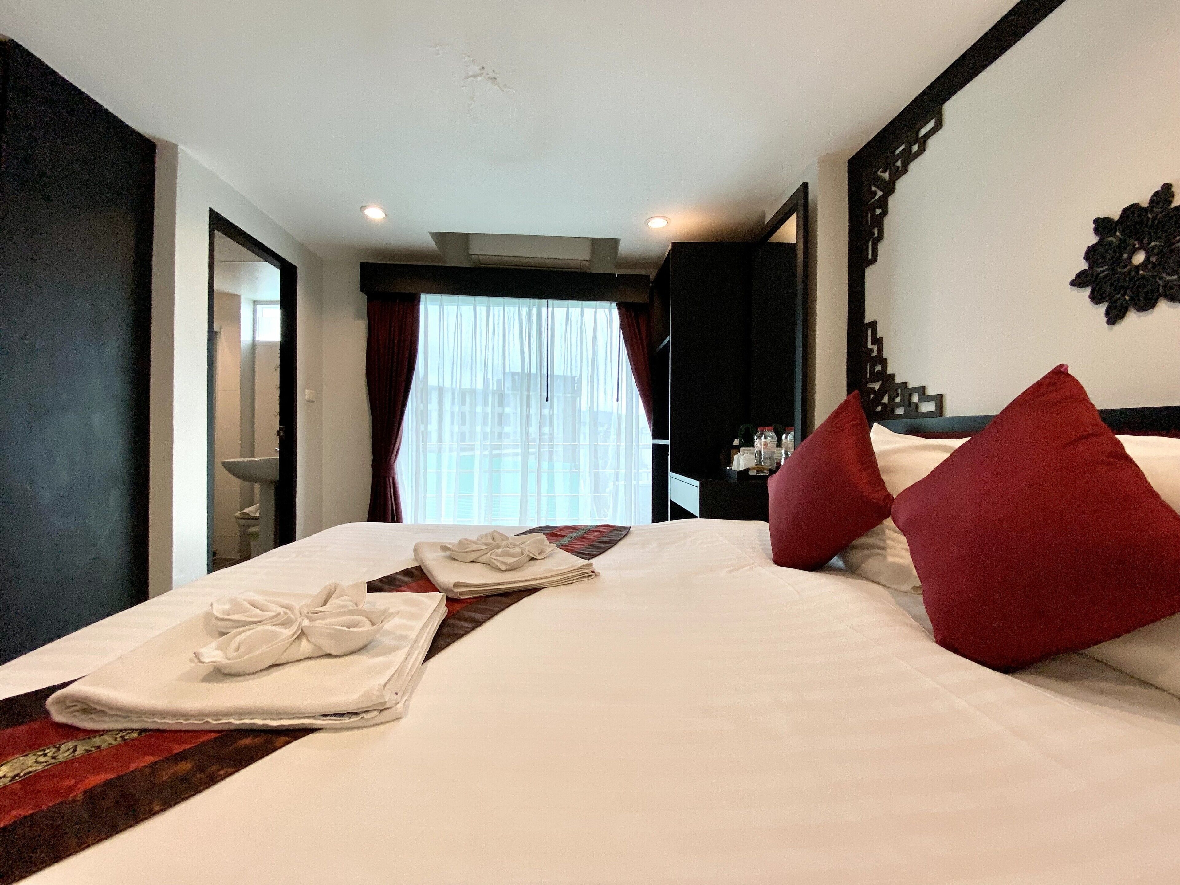 Habitación de hotel con una cama bien hecha, un baño visible a través de una puerta abierta y un amplio ventanal con cortinas.