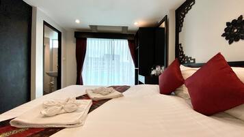 Habitación de hotel con una cama bien hecha, un baño visible a través de una puerta abierta y un amplio ventanal con cortinas.