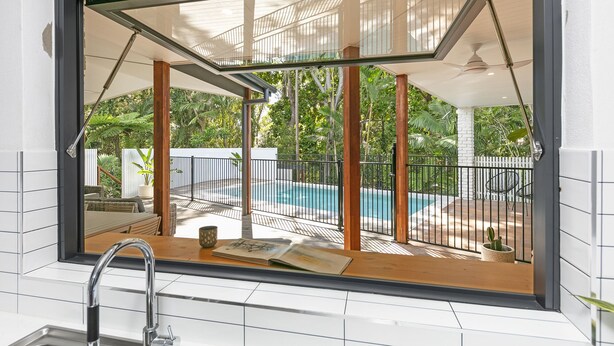 Casa de banho moderna com uma grande janela com vista para uma piscina e vegetação exuberante.