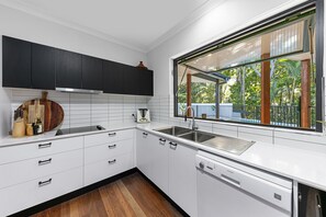 Une cuisine moderne avec des meubles blancs, un plan de travail noir et une fenêtre donnant sur un espace verdoyant.