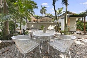 Relax in a tranquil outdoor setting with a round table and two chairs, surrounded by lush greenery and a modern building.