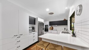 Cozinha moderna com armários brancos, eletrodomésticos de aço inoxidável e uma ilha central com banquetas.