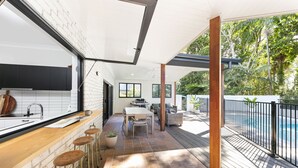 Cozinha moderna com uma grande janela, área de refeições com vista para a piscina e um bar com banquetas.