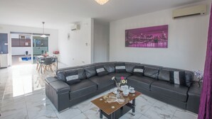 Ett modernt vardagsrum med en mörk lädersoffa, ett glasbord och en tavla med en stadsbild på väggen.