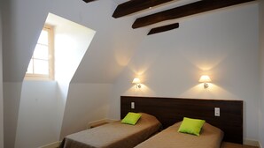 Una habitación con dos camas, cada una con cabecero de madera y almohada verde. Hay dos luces fijadas a la pared, una a cada lado de las camas.