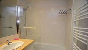 Un baño con lavamanos, espejo, ducha y toallero.