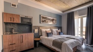 A modern hotel room with a kitchenette, a large bed with multiple pillows, and a view of the outdoors. - Marea Boutique Hotels (Sliema)
