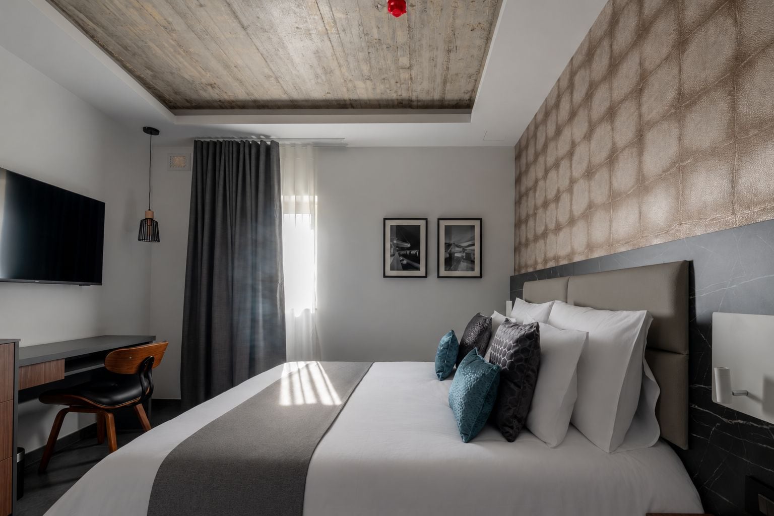 Une chambre d’hôtel moderne dotée d’un grand lit, d’un bureau, d’une chaise, d’une télévision et d’un plafond orné de panneaux en bois.