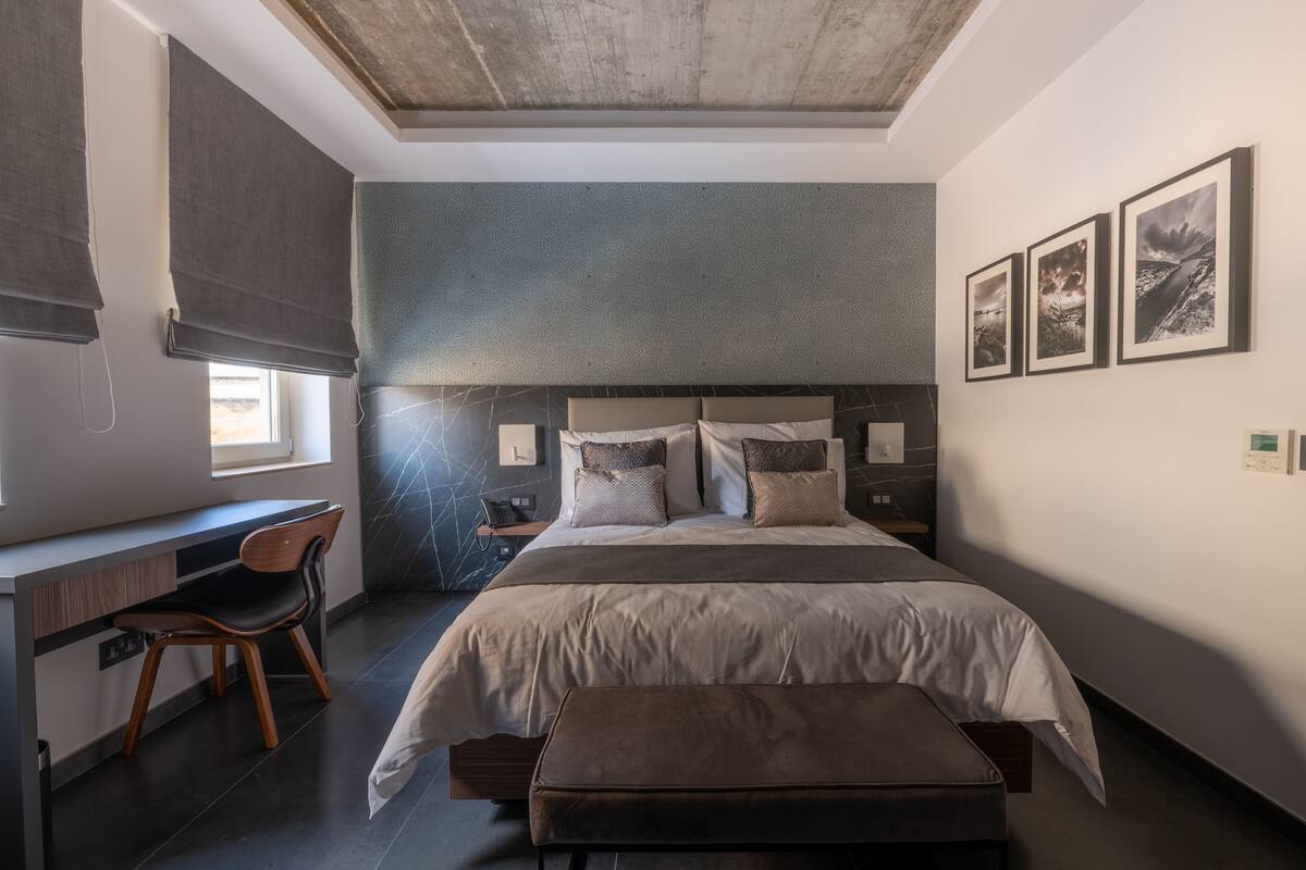 A modern bedroom with a large bed, a desk, and a chair. There are three framed pictures on the wall.