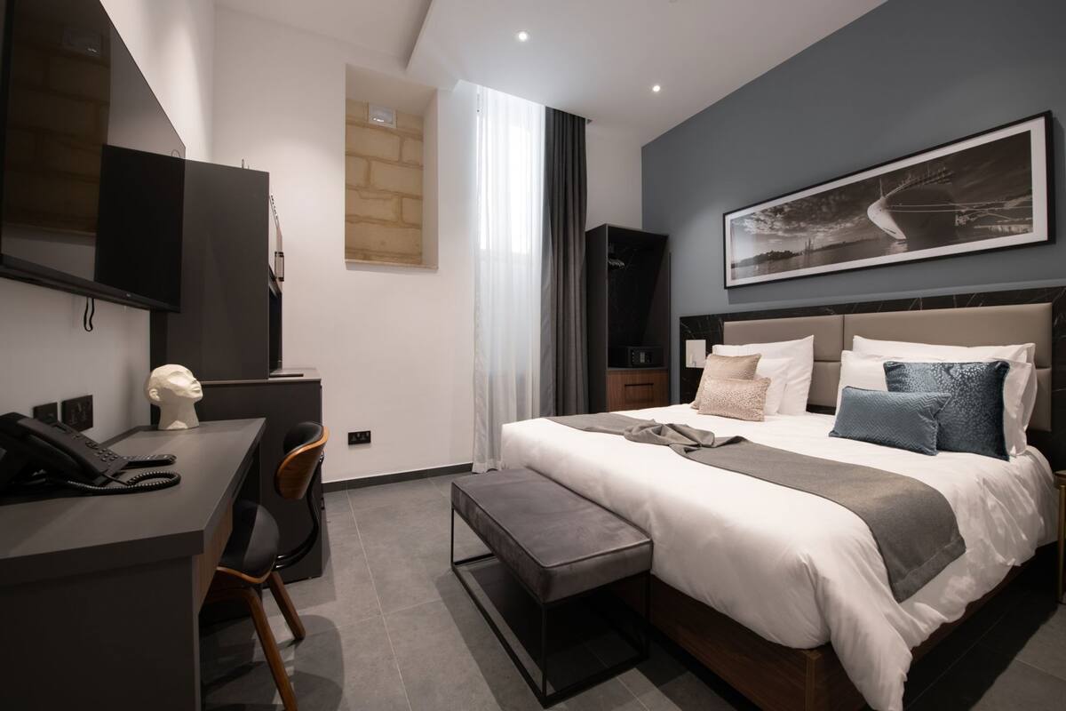 A modern hotel room with a bed, desk, chair, and a large painting on the wall.