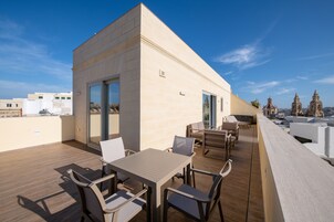 Eine Dachterrasse mit Holzdeck, Sitzgelegenheiten im Freien und Blick auf historische Gebäude.