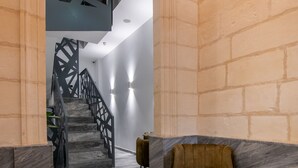 A modern interior with a marble floor, a staircase with geometric railings, a plush armchair, and a small table. - Marea Boutique Hotels (Sliema)