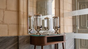 A marble-floored bathroom with a glass-enclosed shower, a wooden vanity with a glass top, and a small stool with a book. - Marea Boutique Hotels (Sliema)