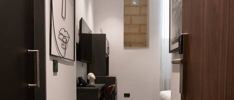 Un couloir moderne avec une porte sombre, un bureau noir avec une chaise, un téléviseur fixé au mur et une œuvre d’art accrochée au mur.