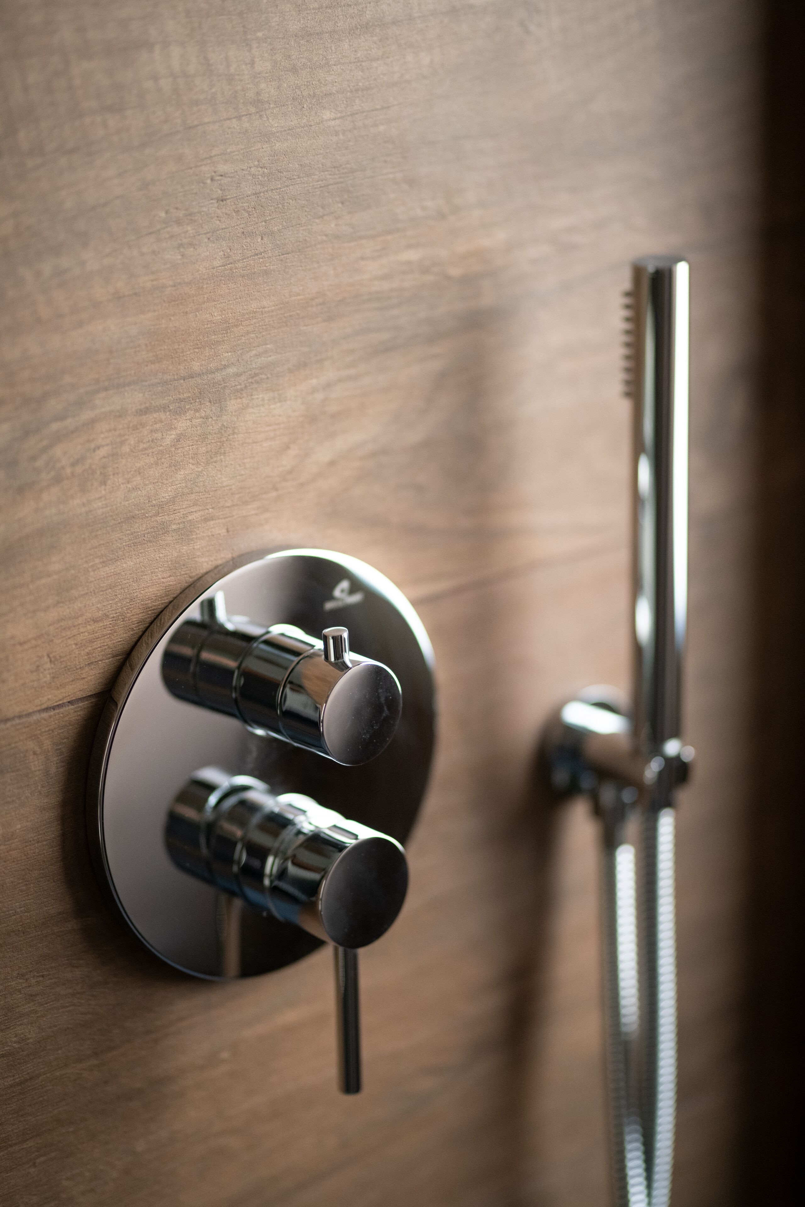 A modern bathroom with a wall-mounted shower control panel and a handheld showerhead.