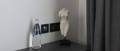 Une pièce moderne avec un bureau en bois foncé, une bouteille en verre transparent, un buste sculpté blanc et un luminaire suspendu noir.