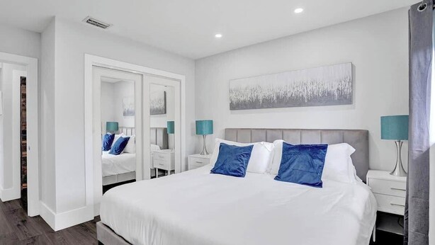 Une chambre à coucher moderne avec un grand lit, des murs blancs et un tableau accroché au-dessus de la tête de lit.