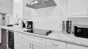 A modern kitchen with white cabinetry, a stainless steel range hood, a built-in oven, a microwave, and a wine cooler.
