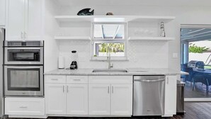 Une cuisine moderne avec des meubles blancs, un four encastré, un lave-vaisselle et une fenêtre au-dessus de l’évier.