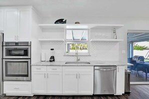 Een moderne keuken met witte kastjes, een ingebouwde oven, een vaatwasser en een raam boven de spoelbak.