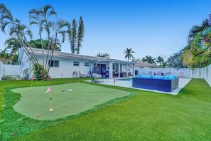 A house with a pool, a covered patio, and a lawn with a golf hole.