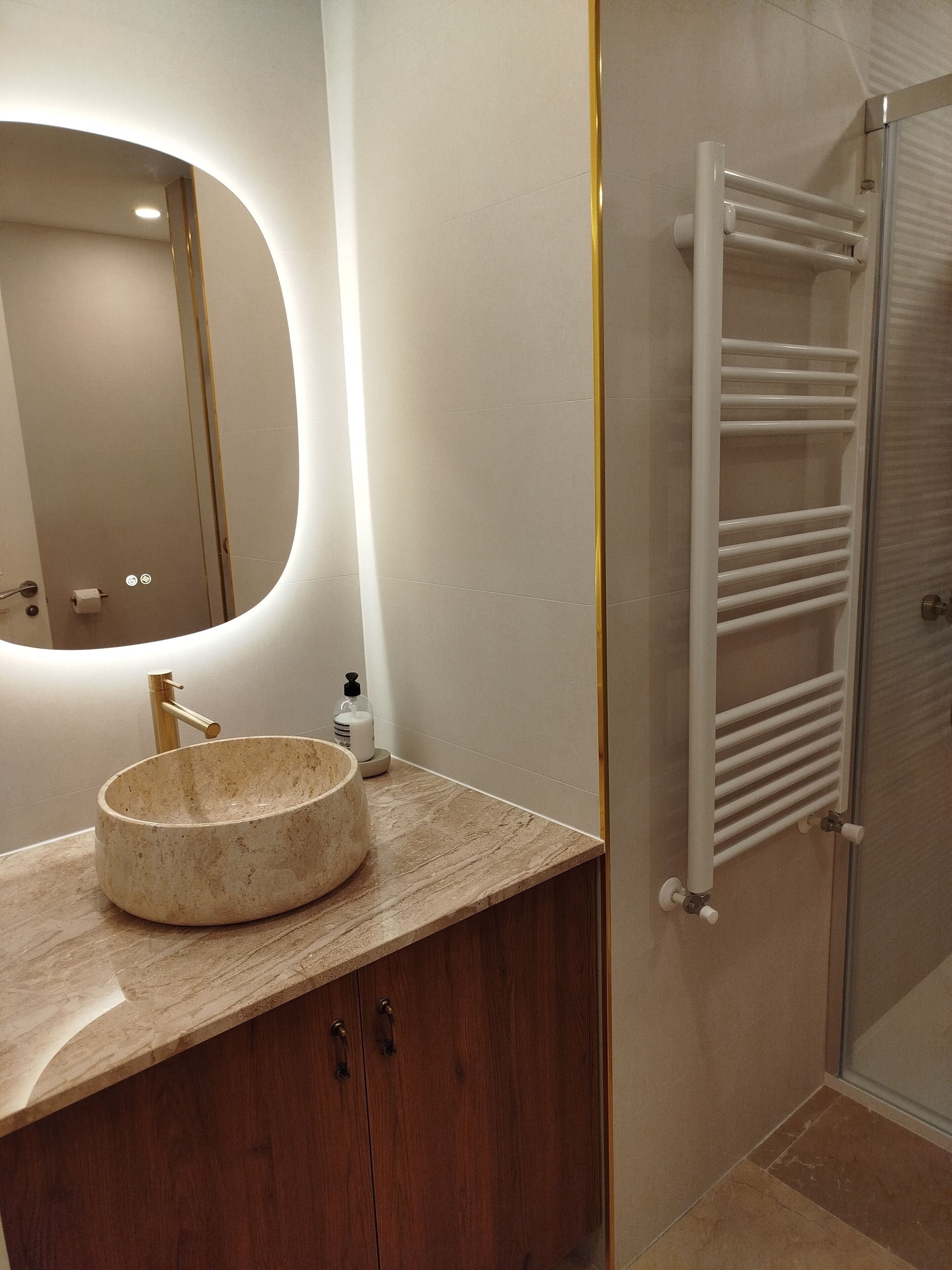 A bathroom with a round sink, a mirror, a towel rack, and a shower area.