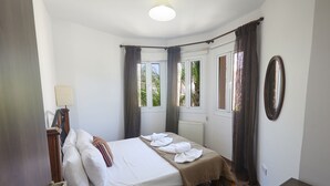 Een slaapkamer met een bed, nachtkastje, raam met gordijnen en een spiegel aan de muur.