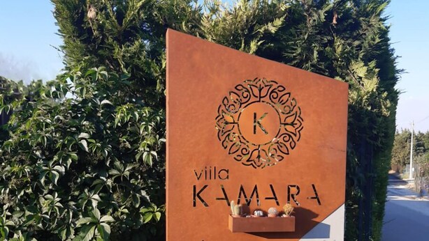 Un panneau indiquant « Villa KAMARA », avec une flèche directionnelle, le tout entouré de verdure.