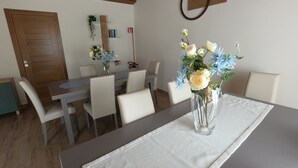 Un coin repas avec une table en bois, des chaises blanches et un vase rempli de fleurs.