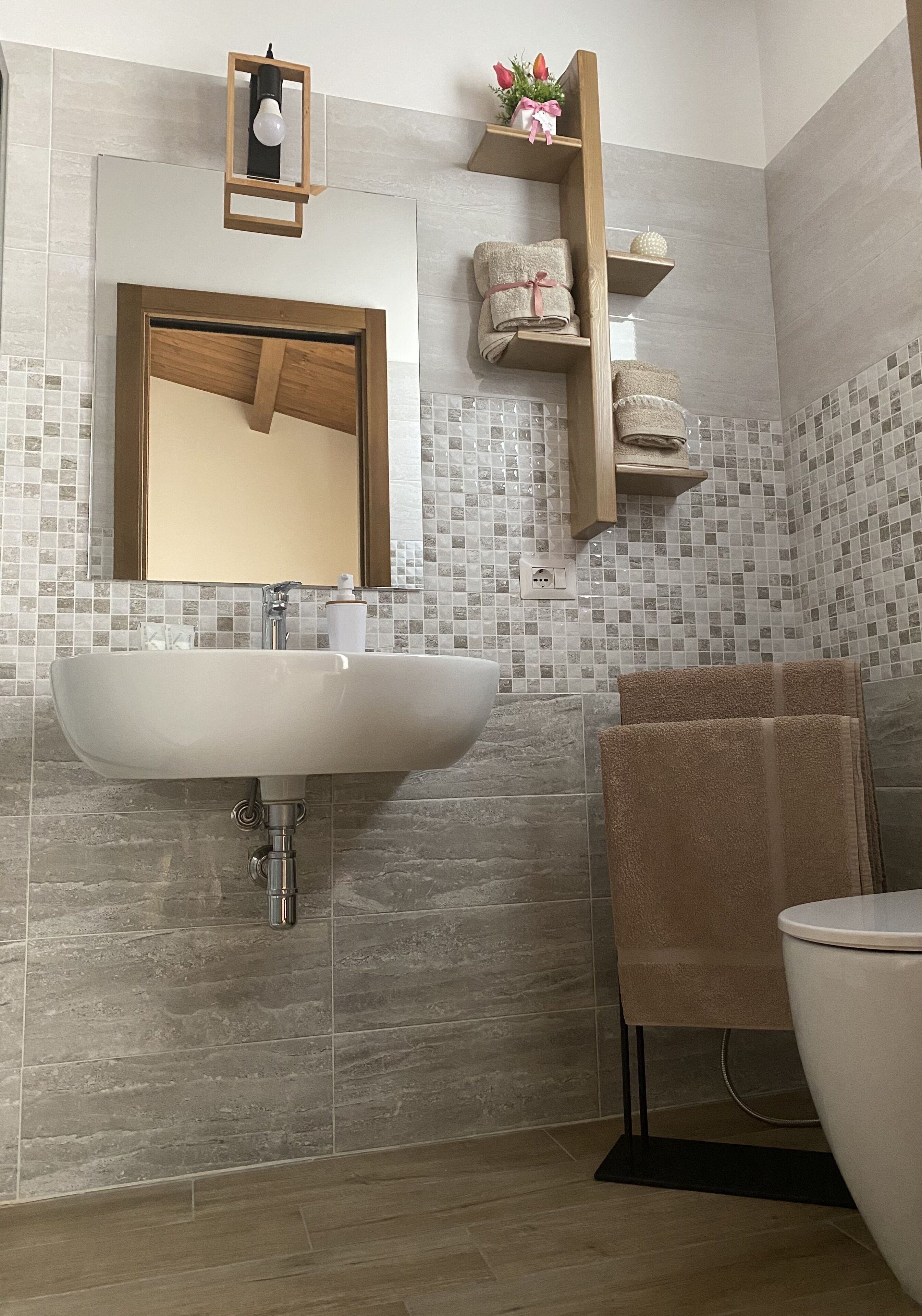 A bathroom with a white sink, a mirror, and a wooden shelf with towels.