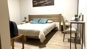 Une chambre d’hôtel avec un lit en bois, un bureau avec une chaise, une petite table et une œuvre d’art accrochée au mur.