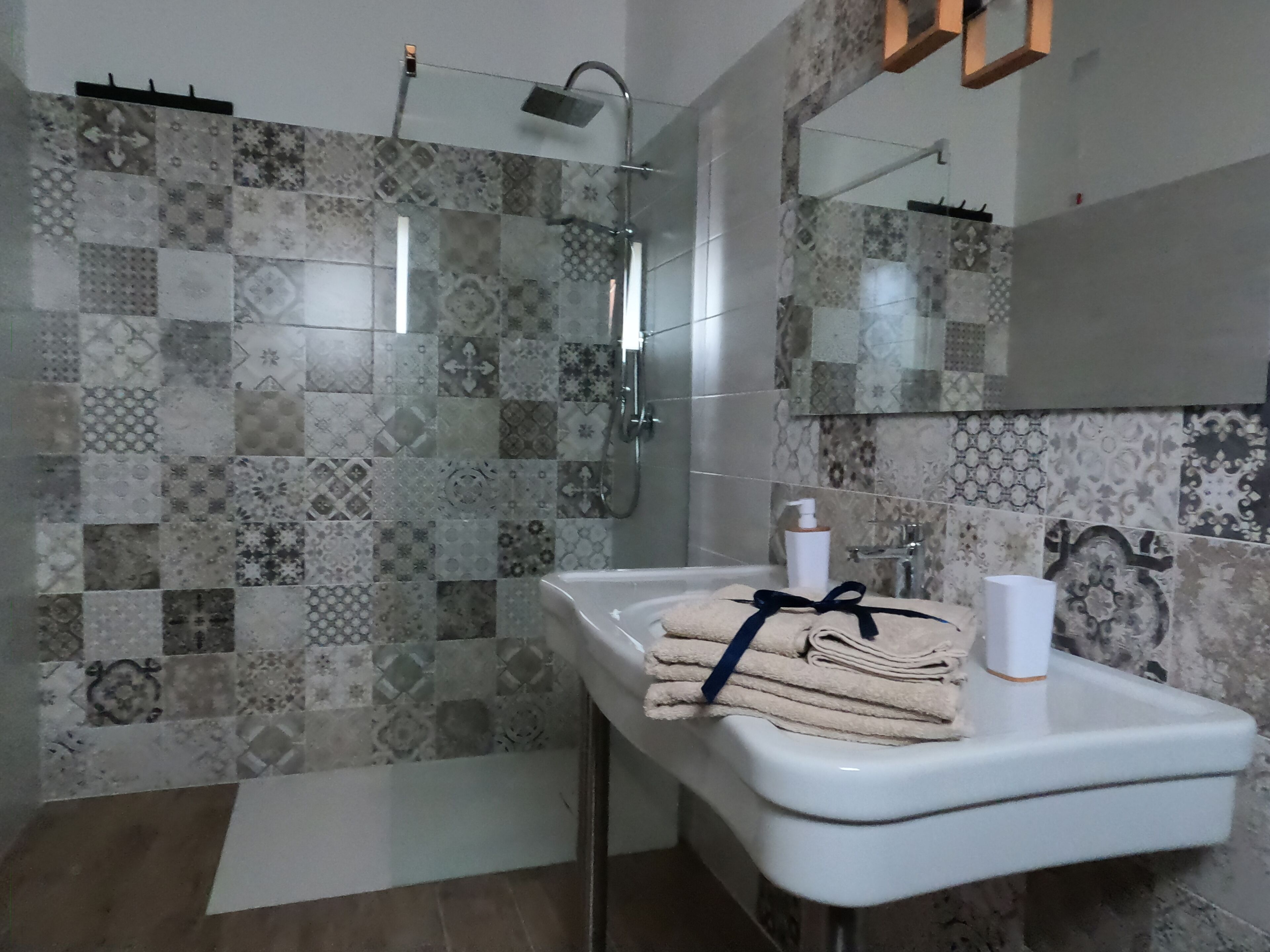 Een badkamer met een betegelde douche, een wastafel met een handdoek en een spiegel.