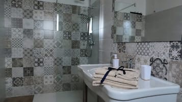 Een badkamer met een betegelde douche, een wastafel met een handdoek en een spiegel.