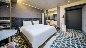 Une chambre d’hôtel avec un grand lit, une armoire, un bureau avec une chaise, un miroir et une salle de bain avec douche.