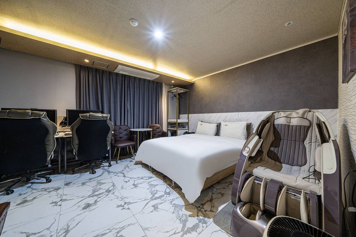 Habitación de hotel con una cama grande, una silla de masaje, un escritorio con una silla y una mesita.