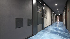 Un couloir doté d’un sol bleu poli, une porte portant l’inscription « Auberge de la Cité Perdue » et une horloge murale.