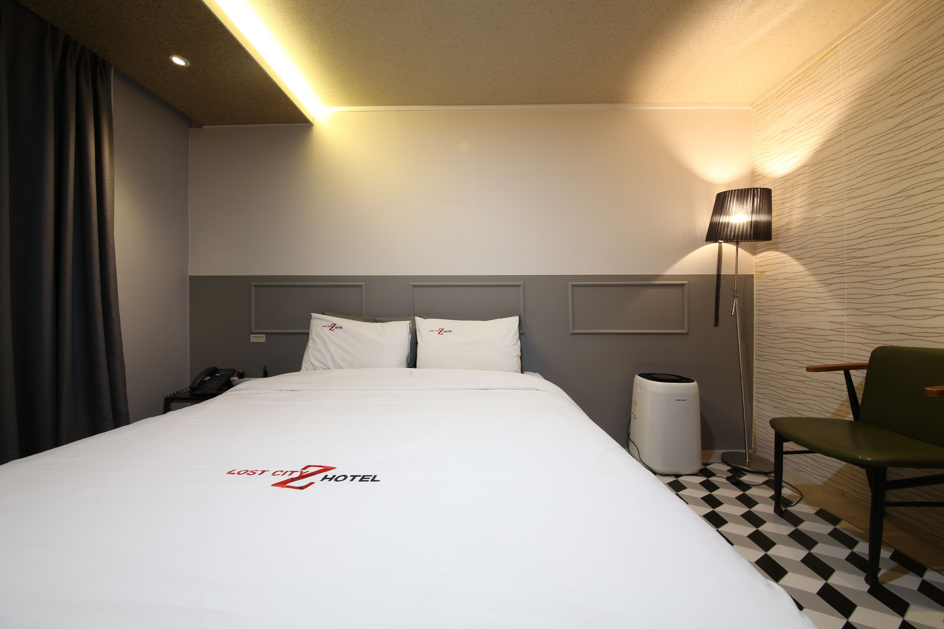 Una habitación de hotel con una cama bien hecha, una silla, una lámpara y un cubo de basura.