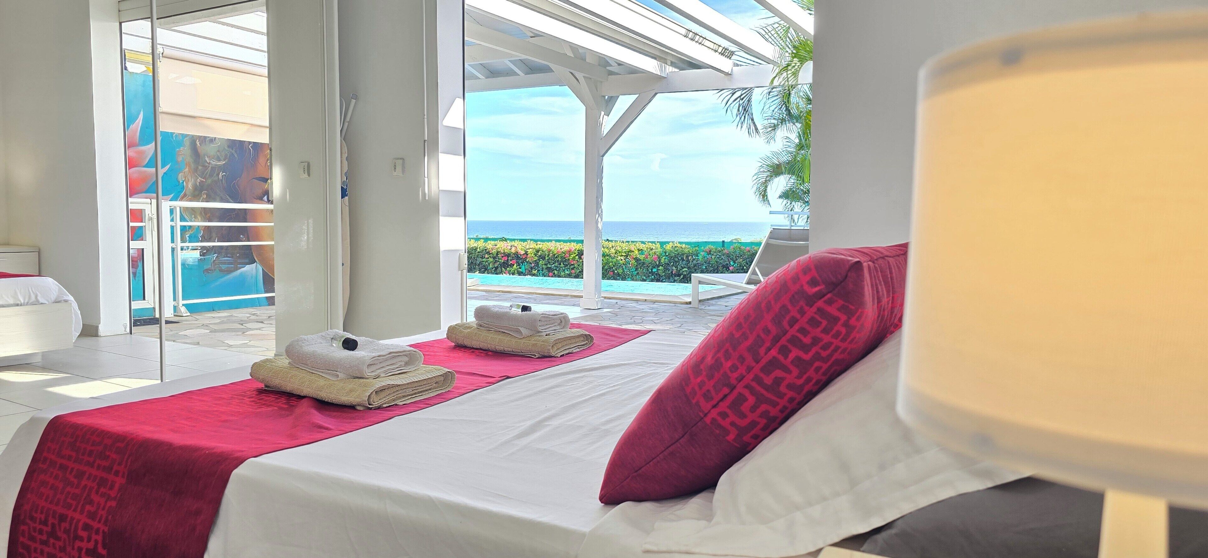 Ein Hotelzimmer mit Bett, einem roten Handtuch, einem weißen Kopfkissen und Meerblick.