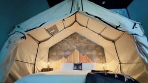 Una habitación tipo tienda de campaña con una cama, dos mesitas de noche y una pared con textura similar a la piedra.