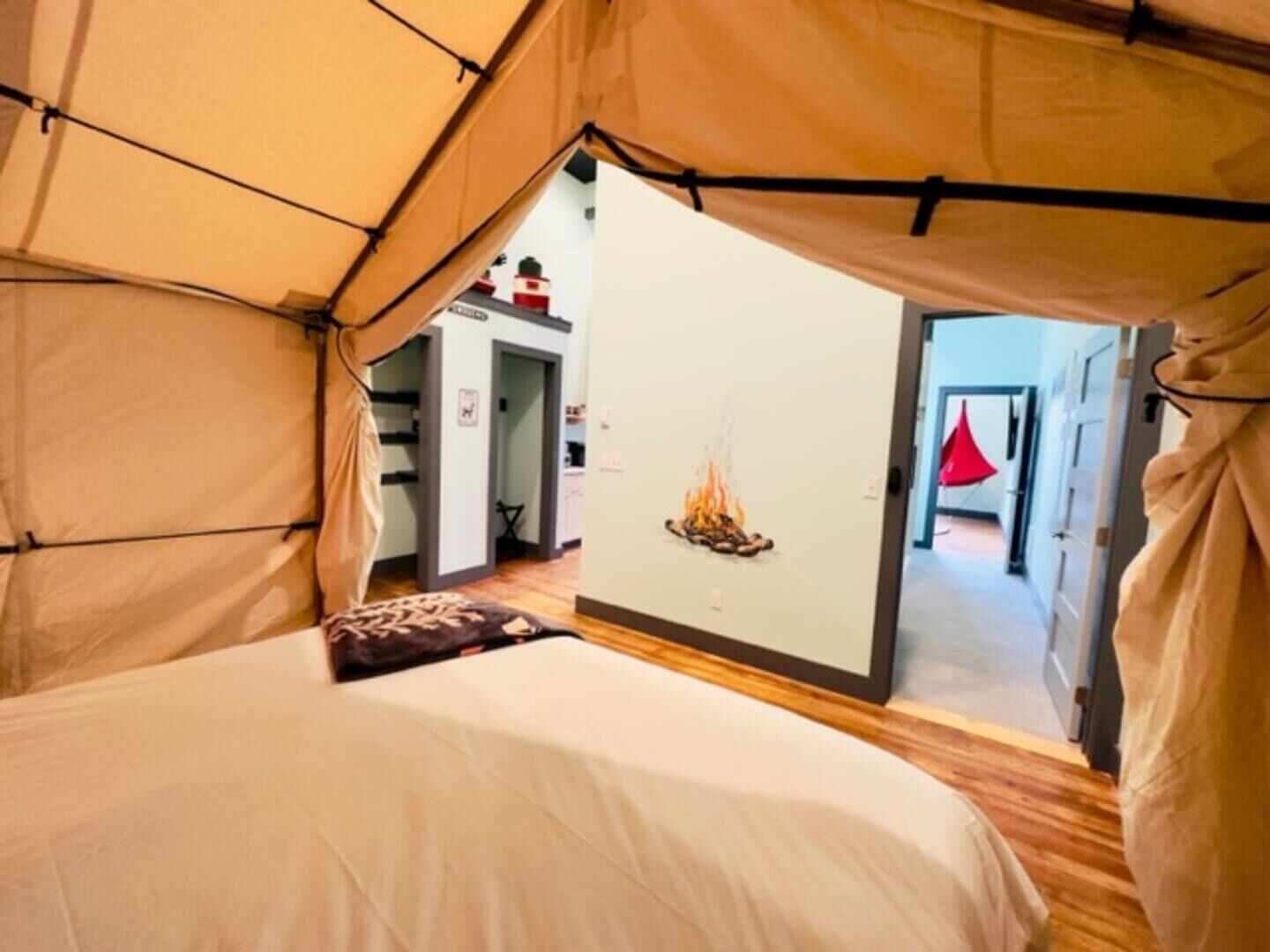 Een tent met een bed, een wandvuur en een gang naar een deur met een rode decoratie.