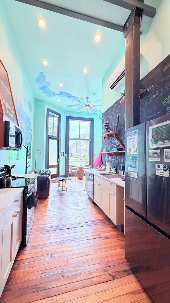 A kitchen with wooden flooring, a ceiling fan, and a view through a large window.