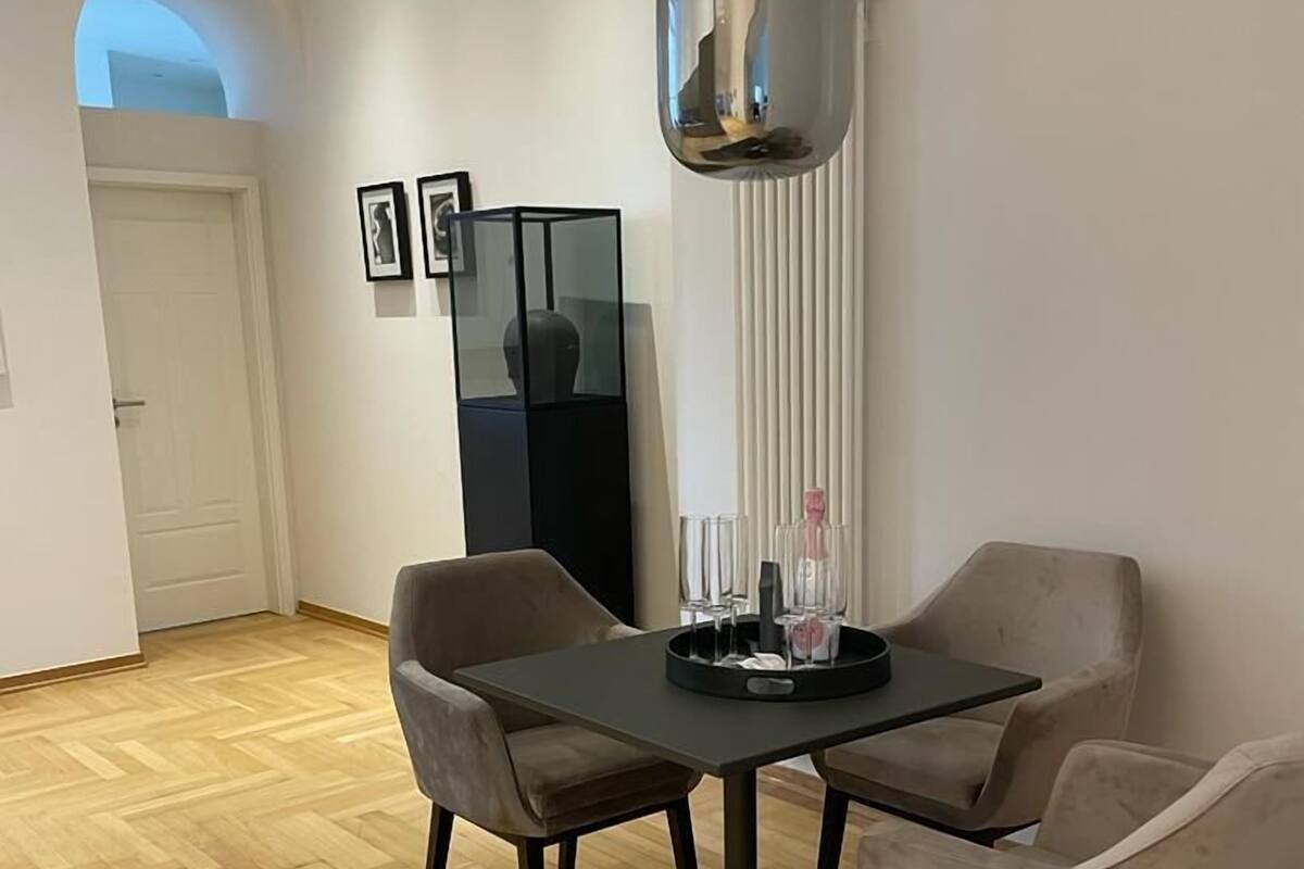 Un comedor con una mesa rectangular, dos sillas, una lámpara colgante moderna y un armario negro.