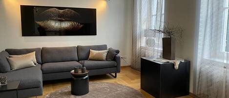 Una sala de estar moderna con un sofá gris, un tapete redondo, una mesa de centro negra y un cuadro abstracto grande en la pared.