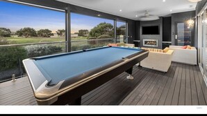 A pool table in a room with large windows, a ceiling fan, and a television. - Beach house on a golf course (Torquay)
