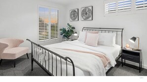 A modern bedroom with a bed, bedside table, and a chair. - Beach house on a golf course (Torquay)