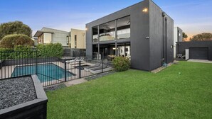 A modern building with a swimming pool, surrounded by a well-maintained lawn and a black fence. - Beach house on a golf course (Torquay)
