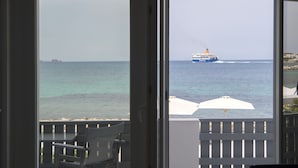 A view from a balcony with a white umbrella and a chair, overlooking a calm sea with a cruise ship in the distance. - Parikia's Seaside House (Paros)