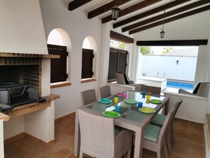 A dining area with a glass table, wicker chairs, and a brick fireplace.