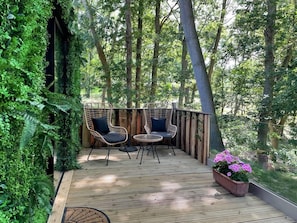 A wooden deck with wicker chairs and a small table, surrounded by lush greenery and trees. - Luxury Cabin in the Woods (Oakham)